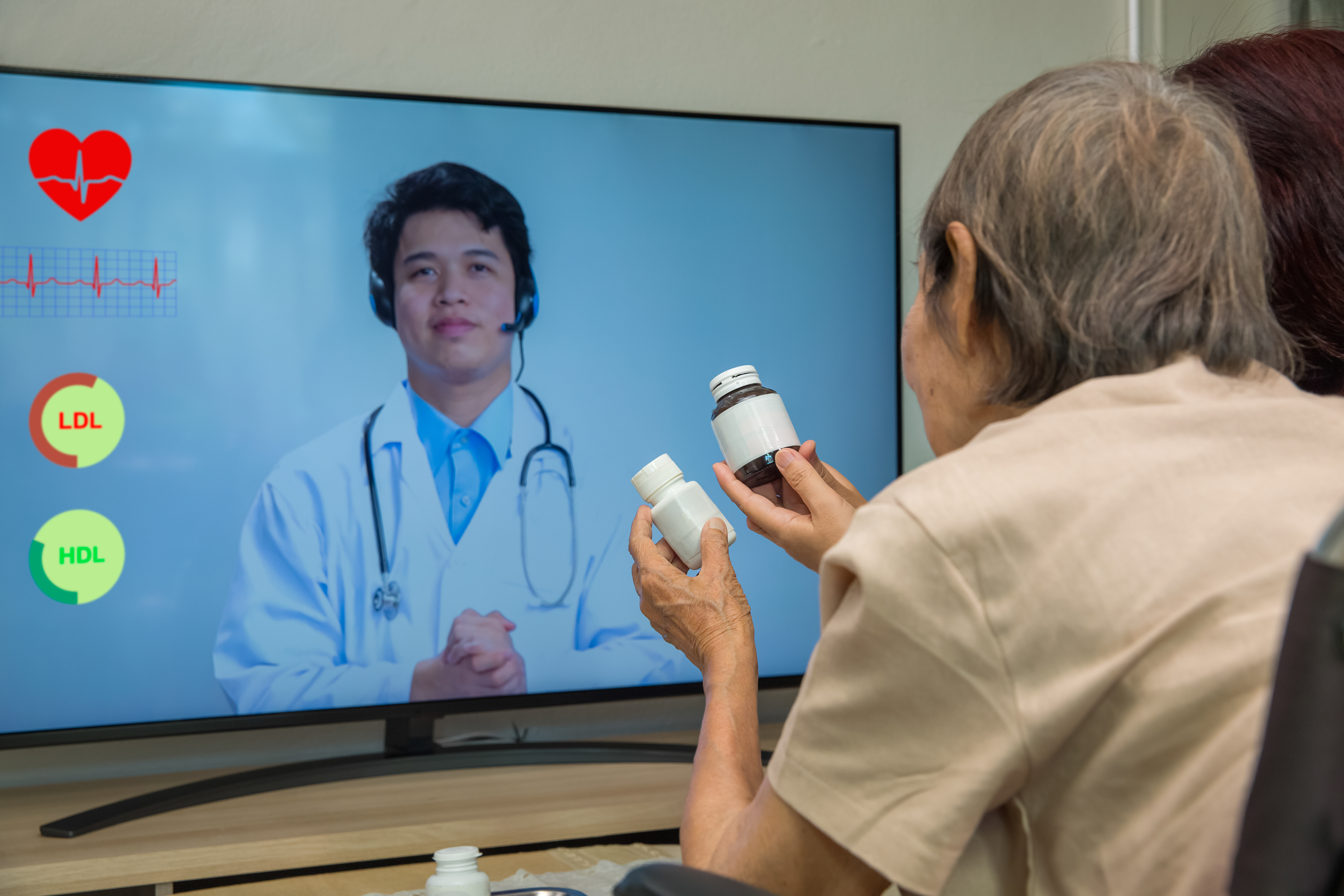 Woman with medication bottles, looking at medical professional on television