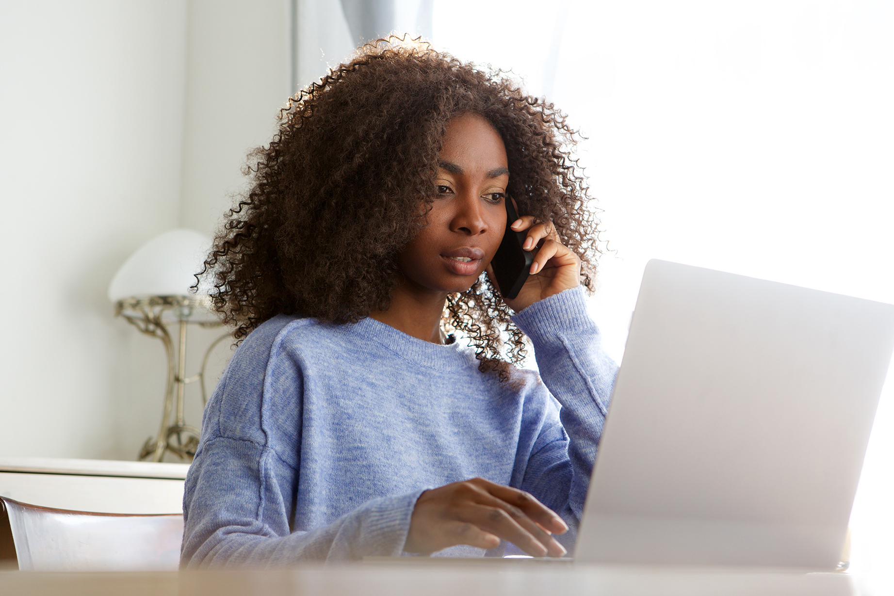 Woman on phone looking at laptop.